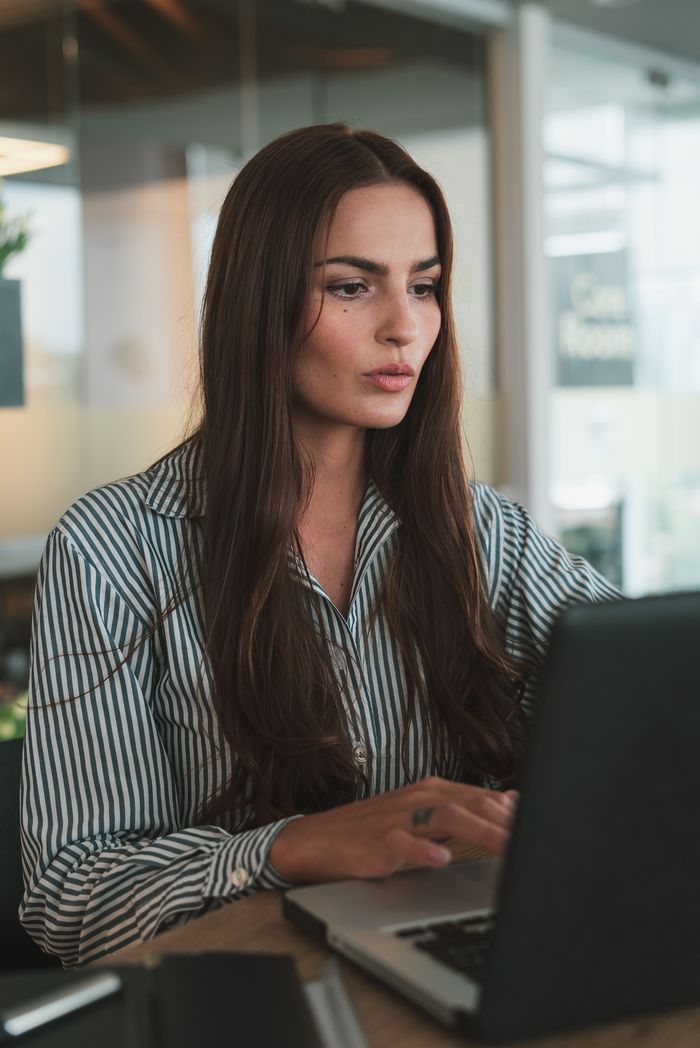 hero Focused businesswoman with long hair working on a laptop in a modern office environment.