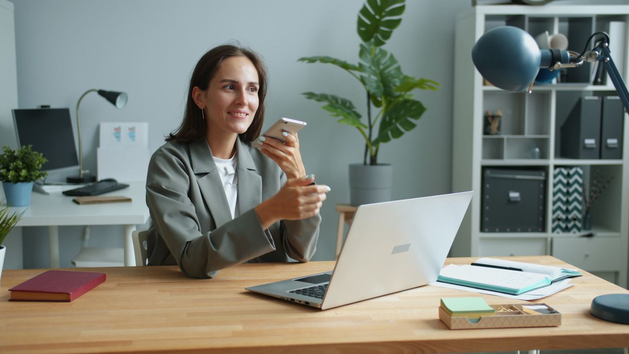 gallery-02 Confident businesswoman using smartphone and laptop in modern office setting.